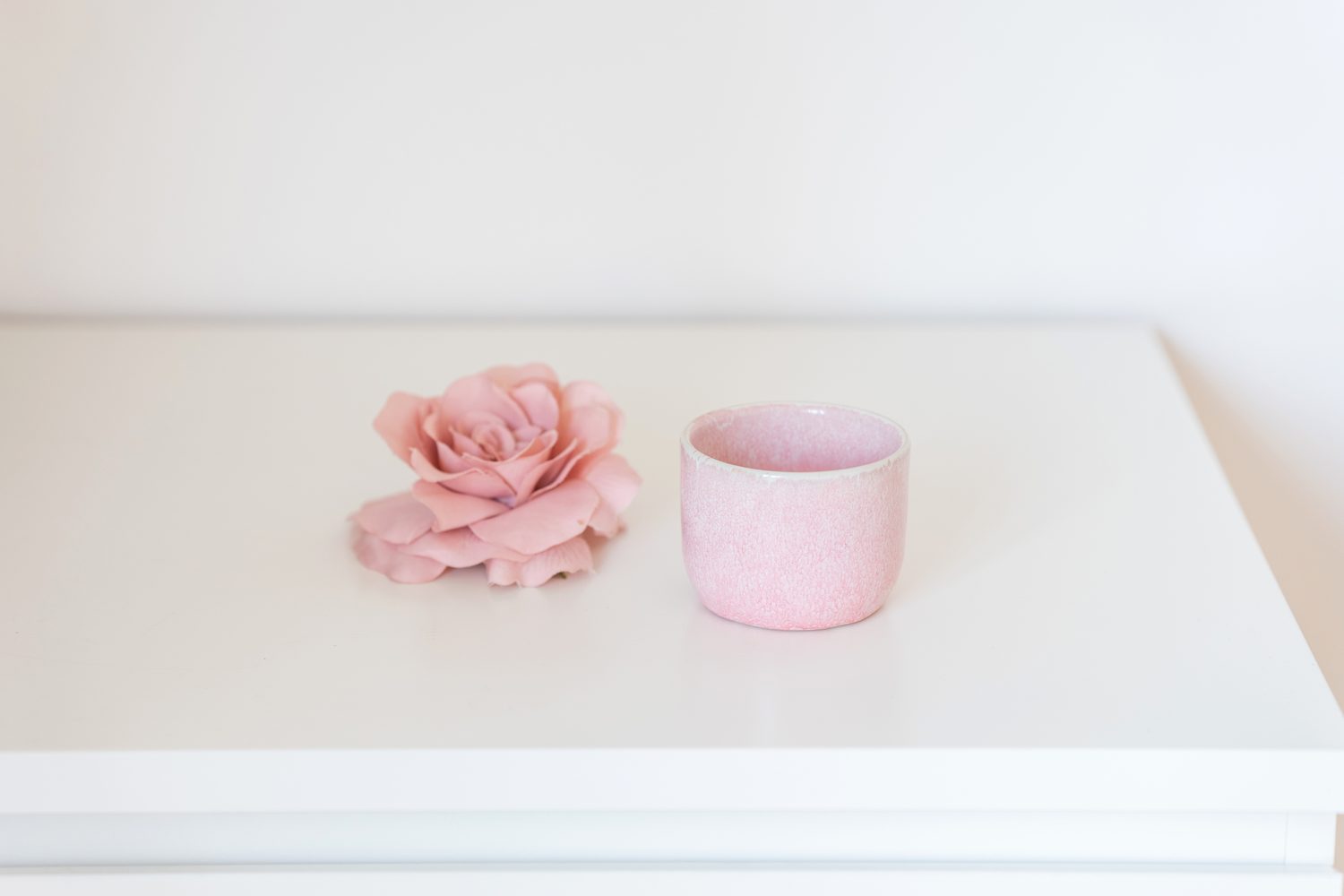 Eine rosa Blüte und eine rosa Teetasse auf weißem Tisch