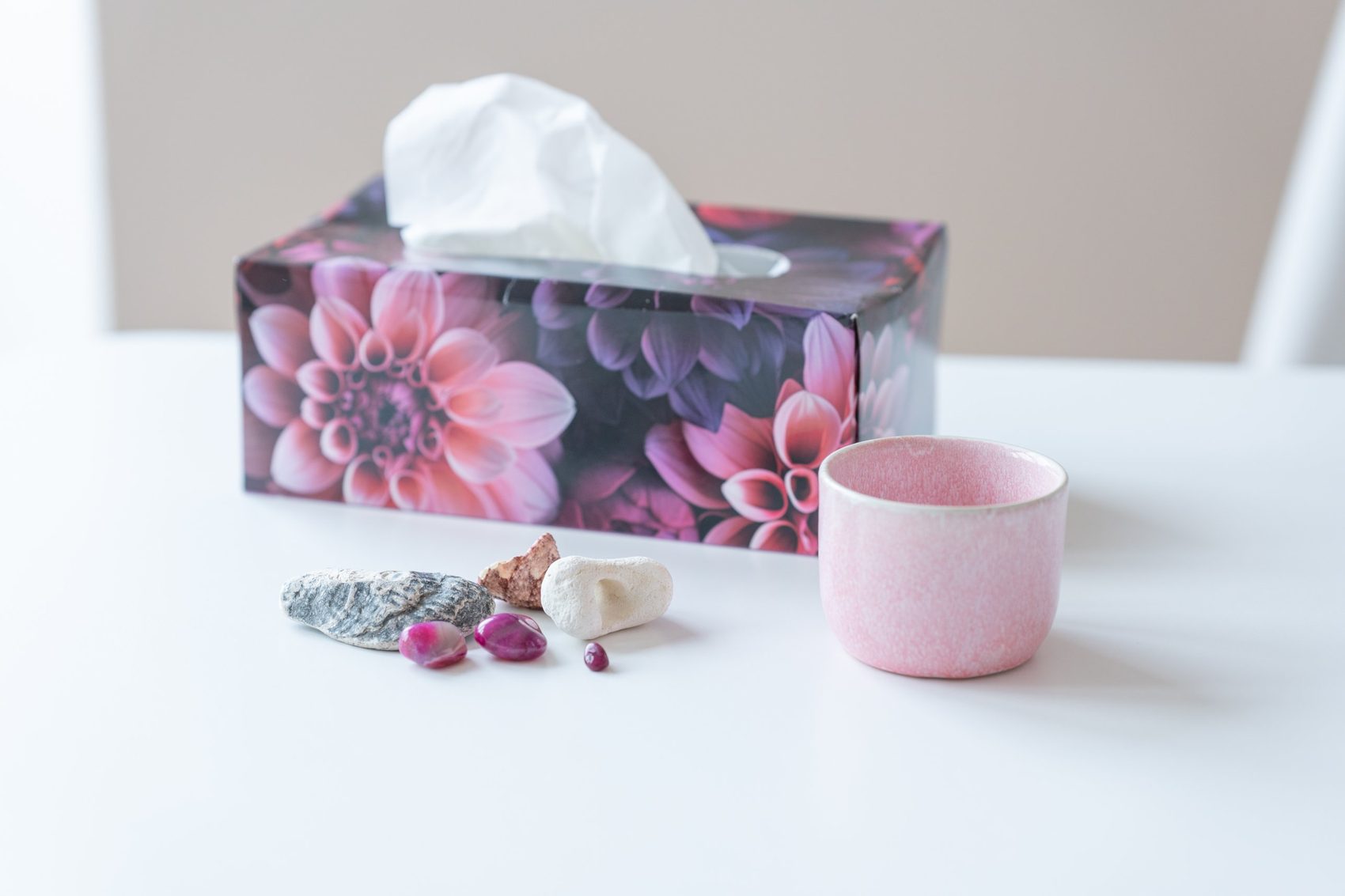 Taschentuchbox, rosa Tasse und Steine auf einem weißen Tisch